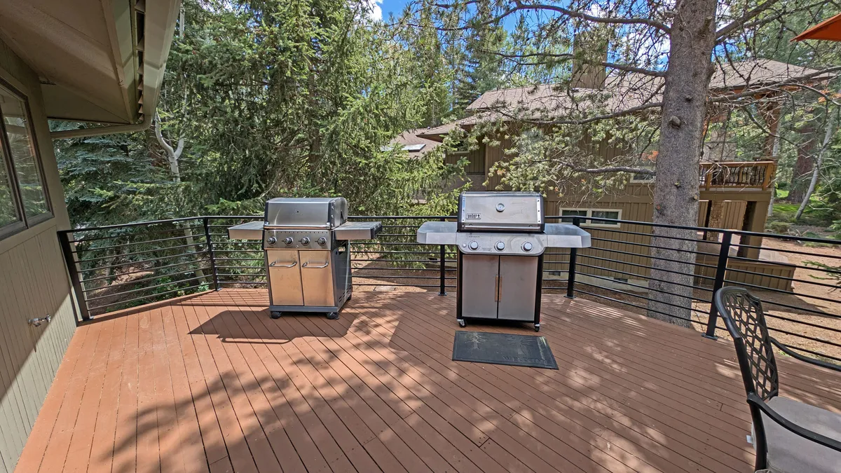 This image showcases two outdoor grills on a spacious deck, surrounded by lush trees and with a sturdy deck railing. The setting suggests a perfect spot for group barbecues and outdoor dining, set against the backdrop of Sunriver's natural beauty.
