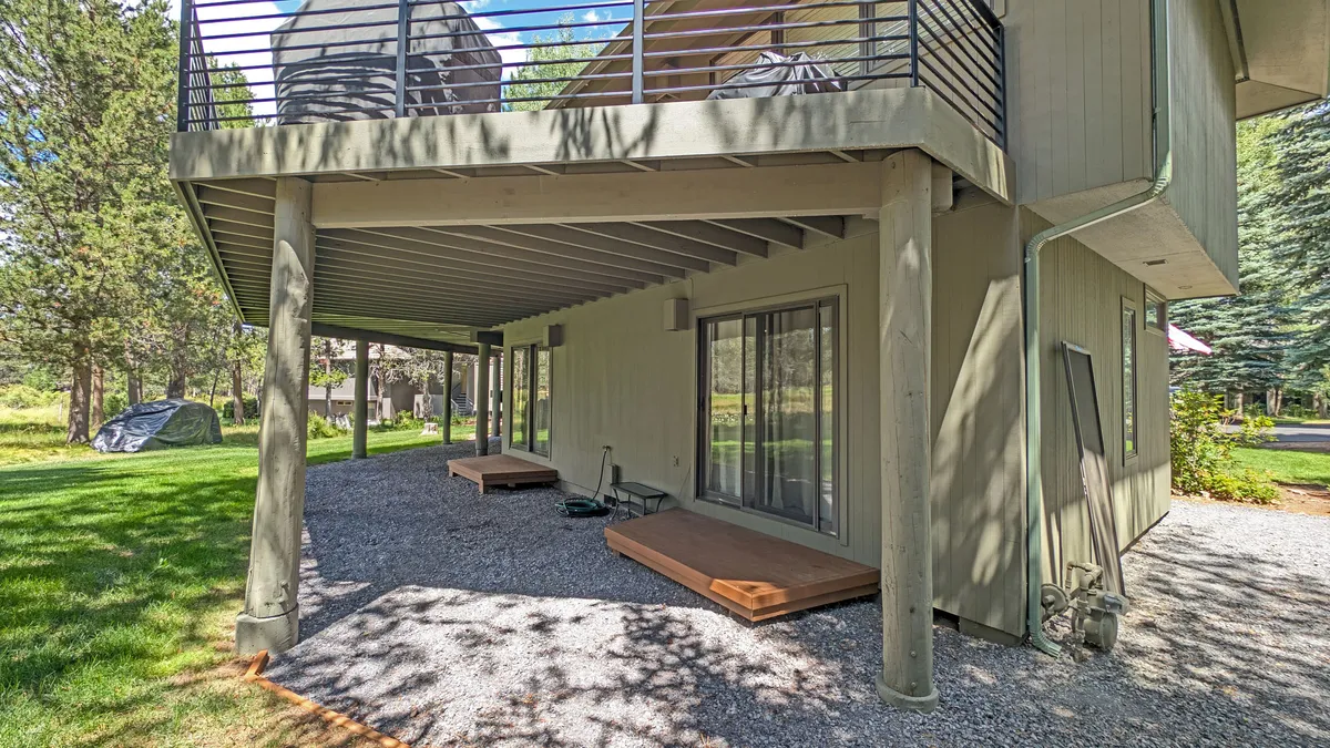 A spacious deck area with large windows looking into the home, a gravel pathway, and a green lawn. The deck is suitable for morning coffee, stargazing, or social gatherings, blending indoor comfort with outdoor enjoyment.