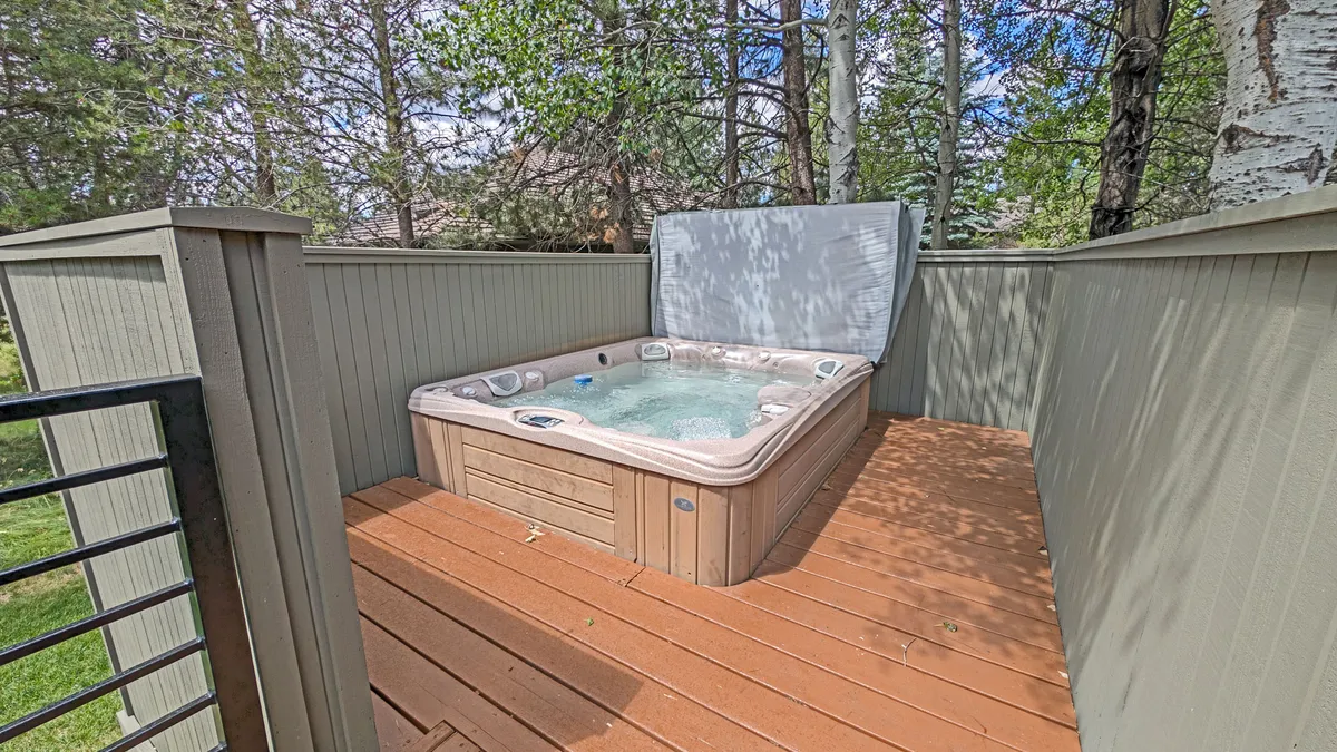 This exterior image features a wooden deck with a private hot tub surrounded by trees, inviting guests to soak and unwind after a day of golf. The tranquil, natural setting emphasizes the comfort and rejuvenation available right outside the home.