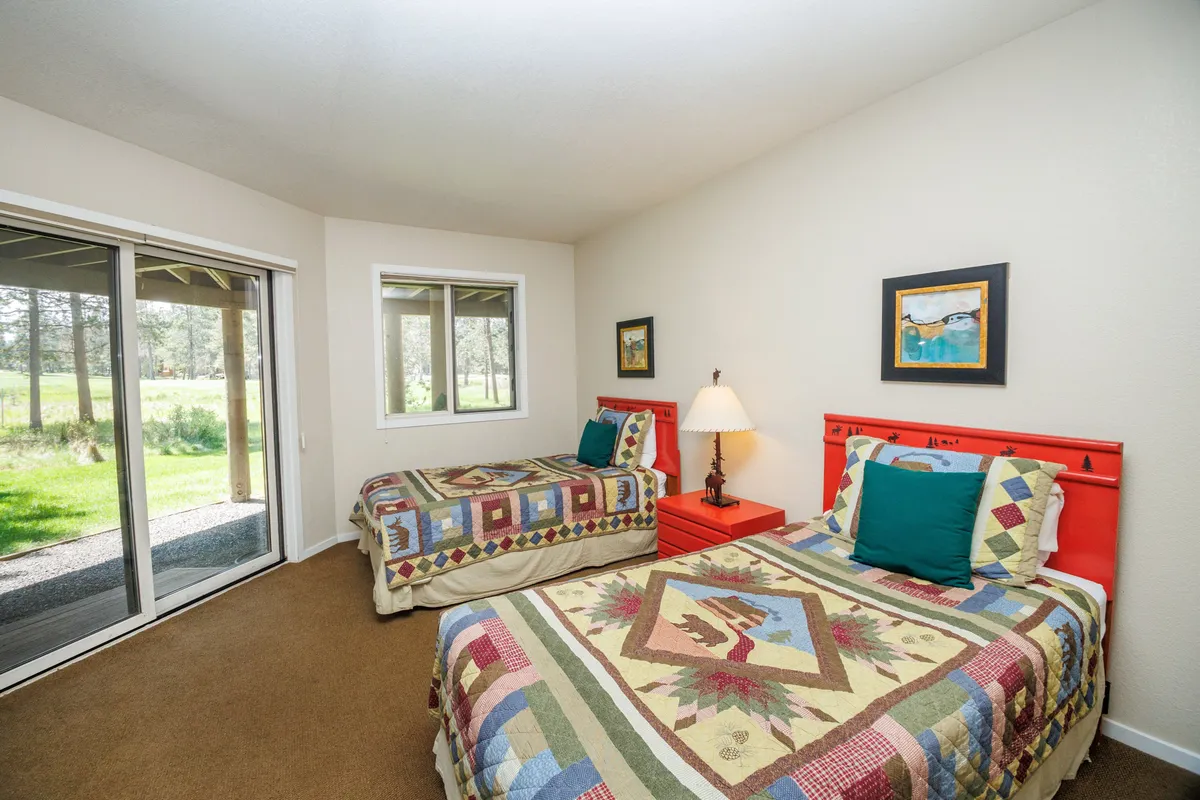 A cozy downstairs bedroom with two twin beds dressed in colorful quilts, situated next to sliding glass doors that open directly to a patio area. The natural light creates a warm and inviting space, and the beds highlight flexible sleeping arrangements.