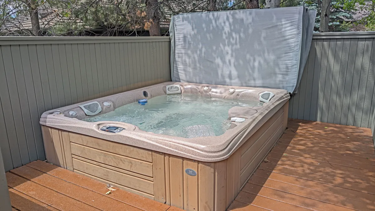 This exterior image features a bubbling hot tub on a wooden deck surrounded by lush greenery, evoking a sense of relaxation and seclusion. The tranquil setting is perfect for unwinding after a day of activities, with sunset views that add a touch of resort-style luxury.