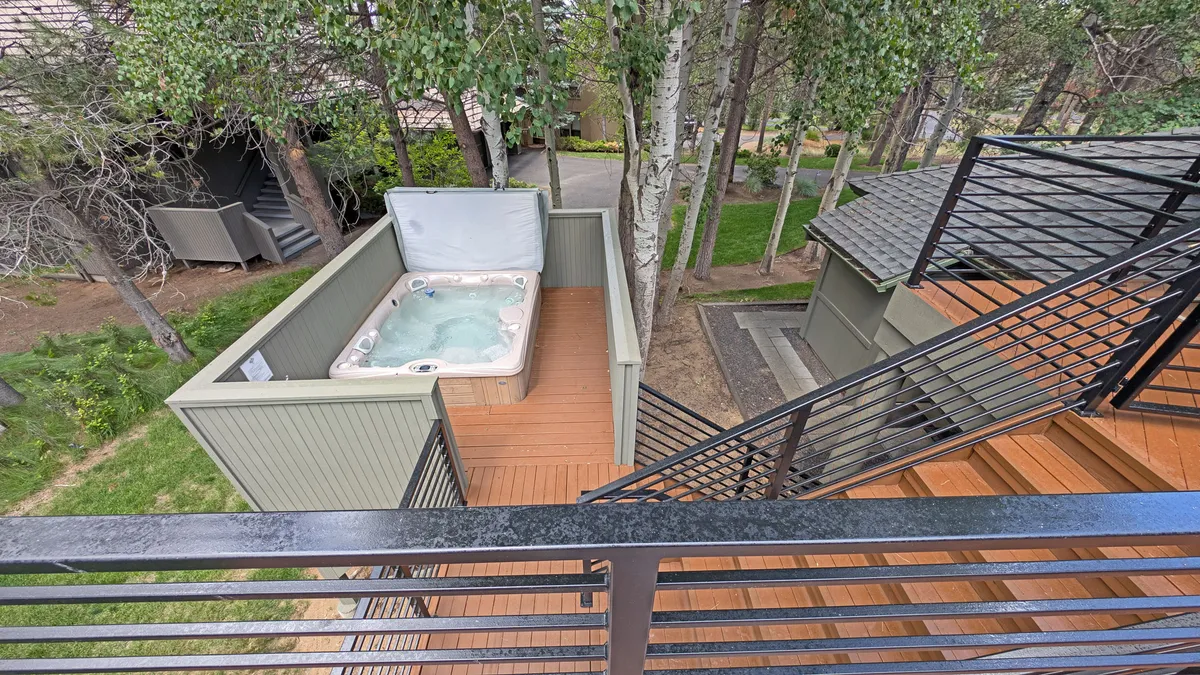 This inviting exterior scene shows a hot tub nestled on a spacious wooden deck, surrounded by tall trees. The area is perfect for morning coffee or evening relaxation, emphasizing both privacy and connection with nature.