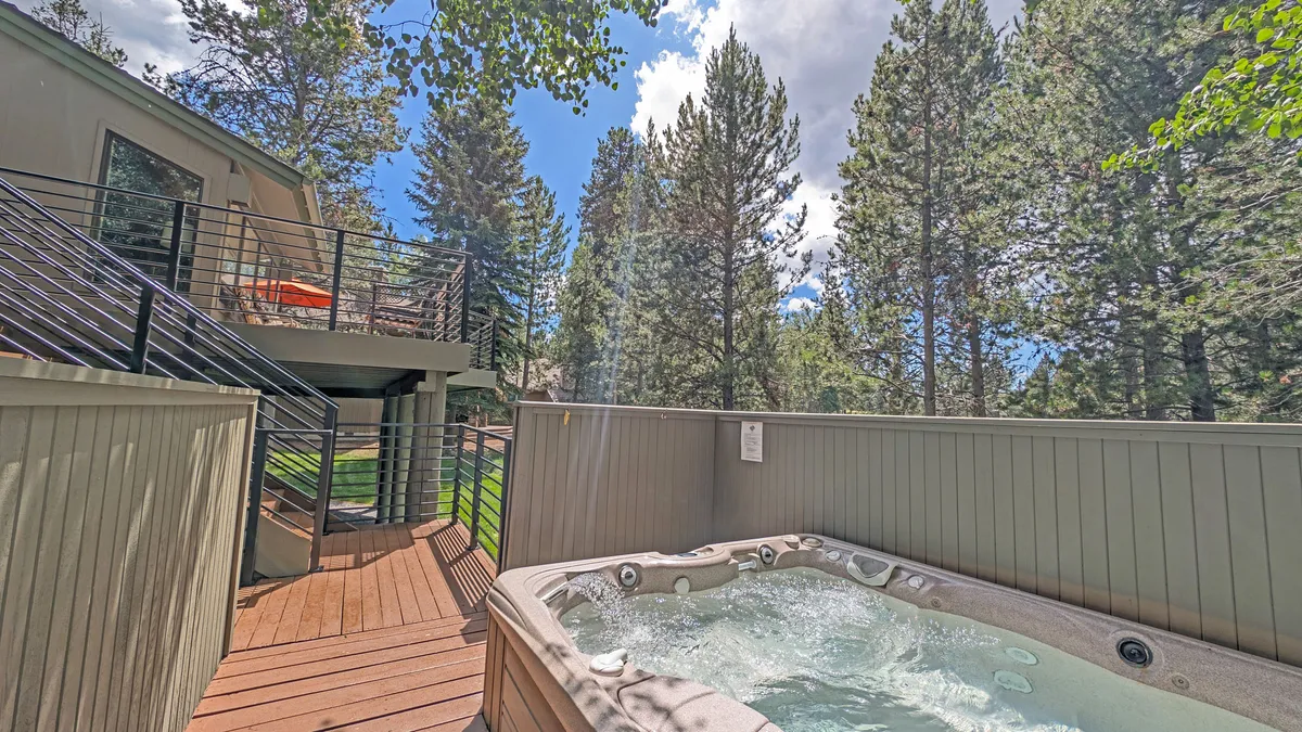 This image showcases the private hot tub nestled on the edge of a spacious wooden deck, surrounded by tall trees and overlooking the natural beauty beyond. The deck is visible with seating areas inviting relaxation, and the tranquil atmosphere is enhanced by the soft lighting, suggesting either a starlit night or a peaceful morning.