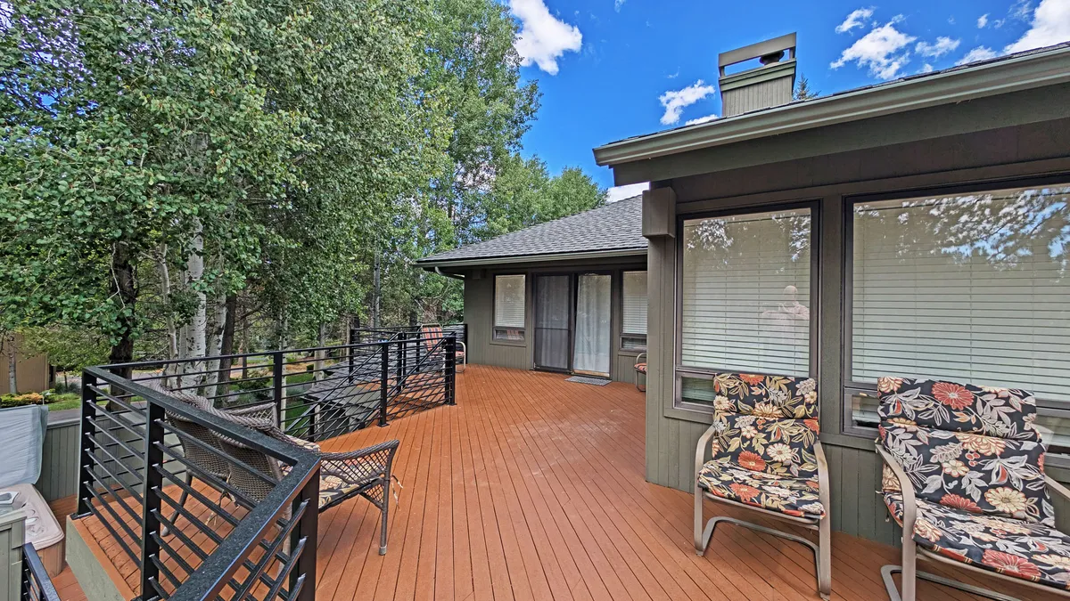 A tranquil wooden deck surrounded by lush greenery, featuring comfortable chairs that invite guests to sit and enjoy the outdoors. The deck offers sunset views and a peaceful setting for conversation or relaxation after a day of activities.